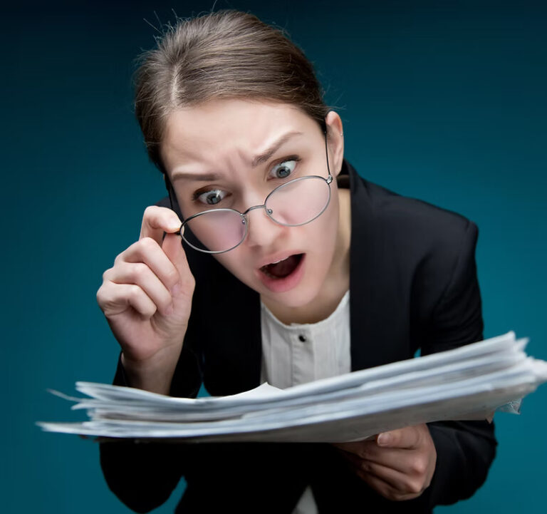 A young woman puts glasses on her nose and looks at documents with angry surprise_ Directo